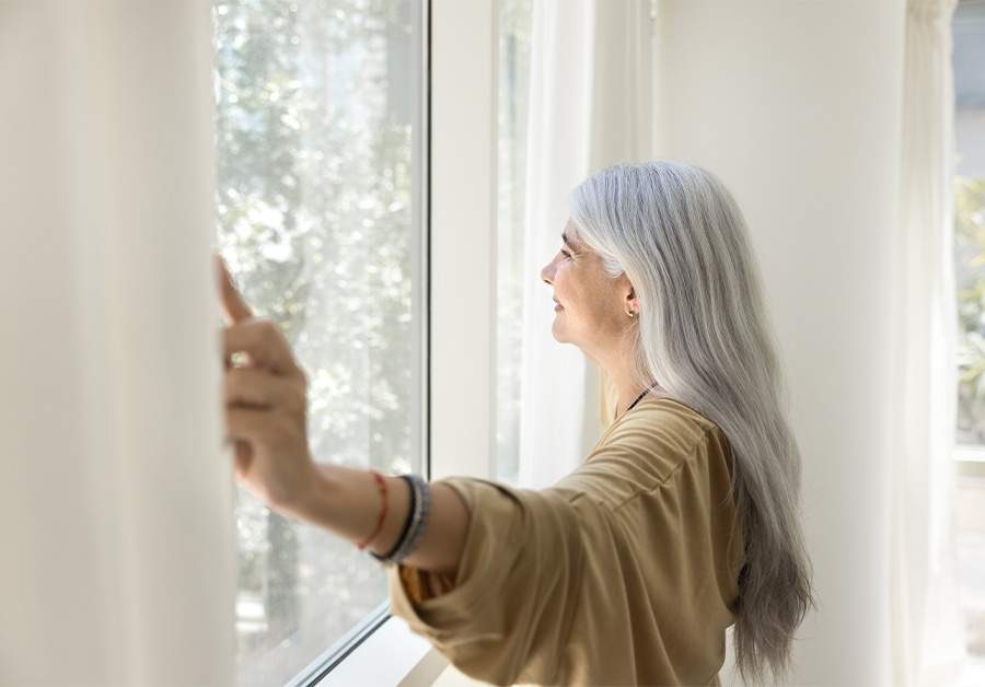 Happy inspired senior Latin woman opening white transparent shades